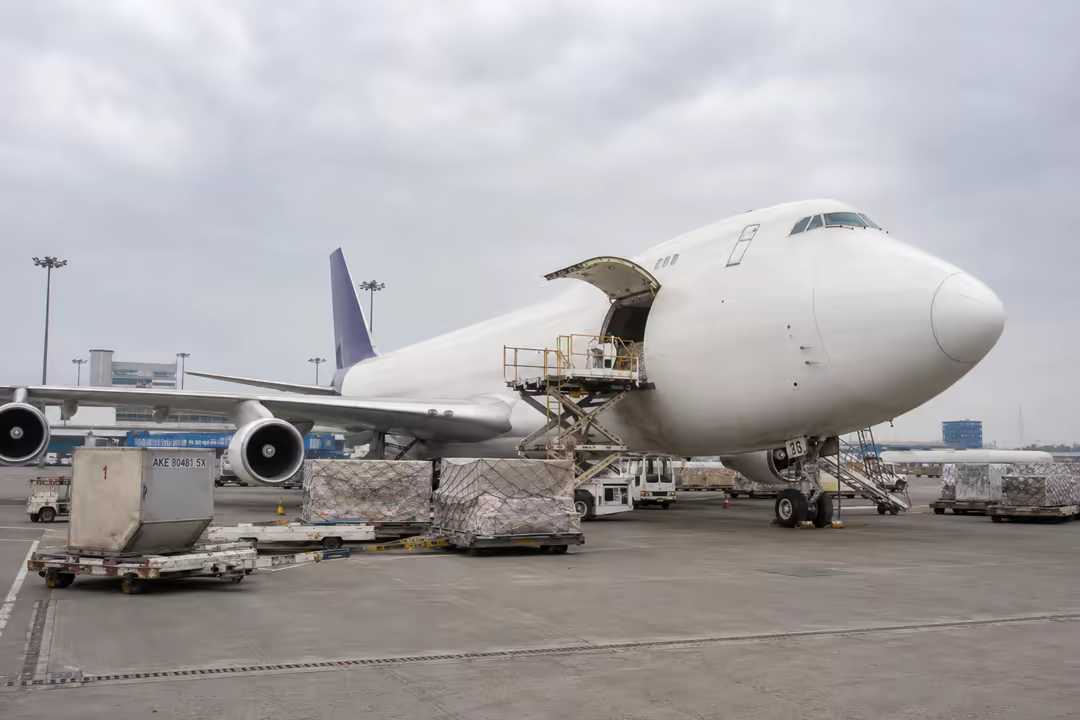 Wide-body freighter with its nose door open, being loaded on the apron